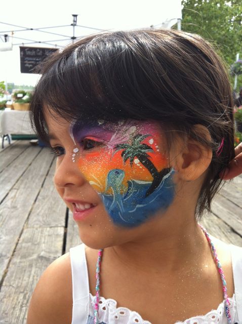 A smiling little girl wears a bright and colourful sunset face paint