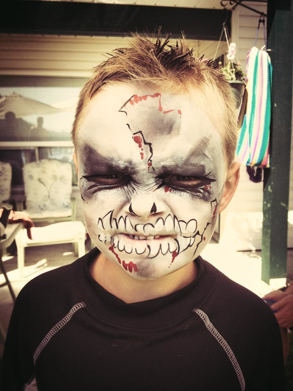 A grimacing little boy wears a white, black and red zombie face paint
