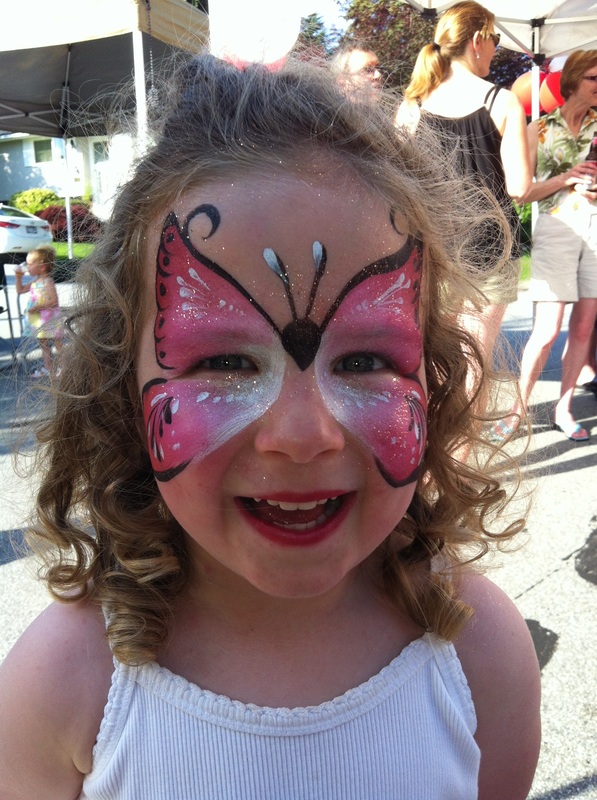 A smiling little girl wears pink butterfly face paint