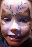A smiling child wear reindeer face paint with a little red nose