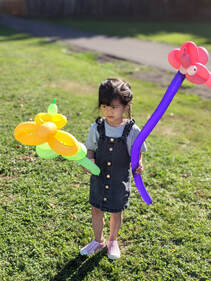 A little girl holding a yellow flower balloon and a pink dog balloon animal