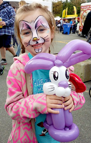 Little girl with Easter Bunny face paint holding a purple and white Easter bunny balloon