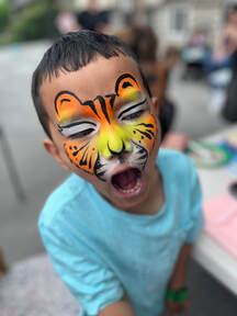 Little boy making a roaring face with orange, yellow, and black tiger face paint