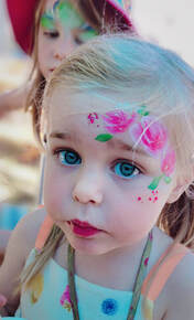 Little girl with braids wearing pink face paint roses above her eye