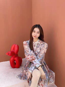 A smiling woman wearing a dress sits next to a red balloon animal statue