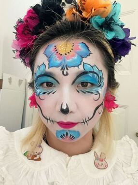 A woman wearing a flower crown with Day of the Dead face paint on her face