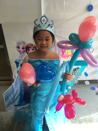 A little girl wearing a Queen Elsa dress holds 2 heart balloons and a heart wand made of balloons