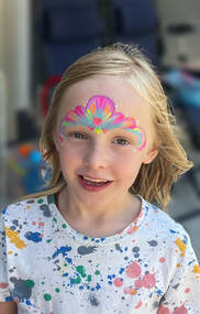A little girl smiling and looking into the camera wearing colourful mermaid face paint