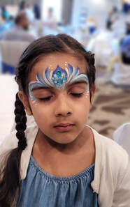 Little girl with braids closing her eyes with blue and white sparkly princess face paint