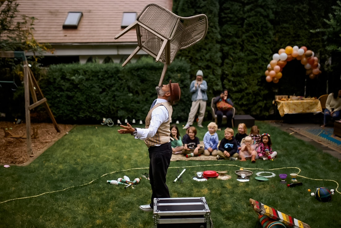 A crowd of children watch a magician balancing a chair on his chin at a birthday party