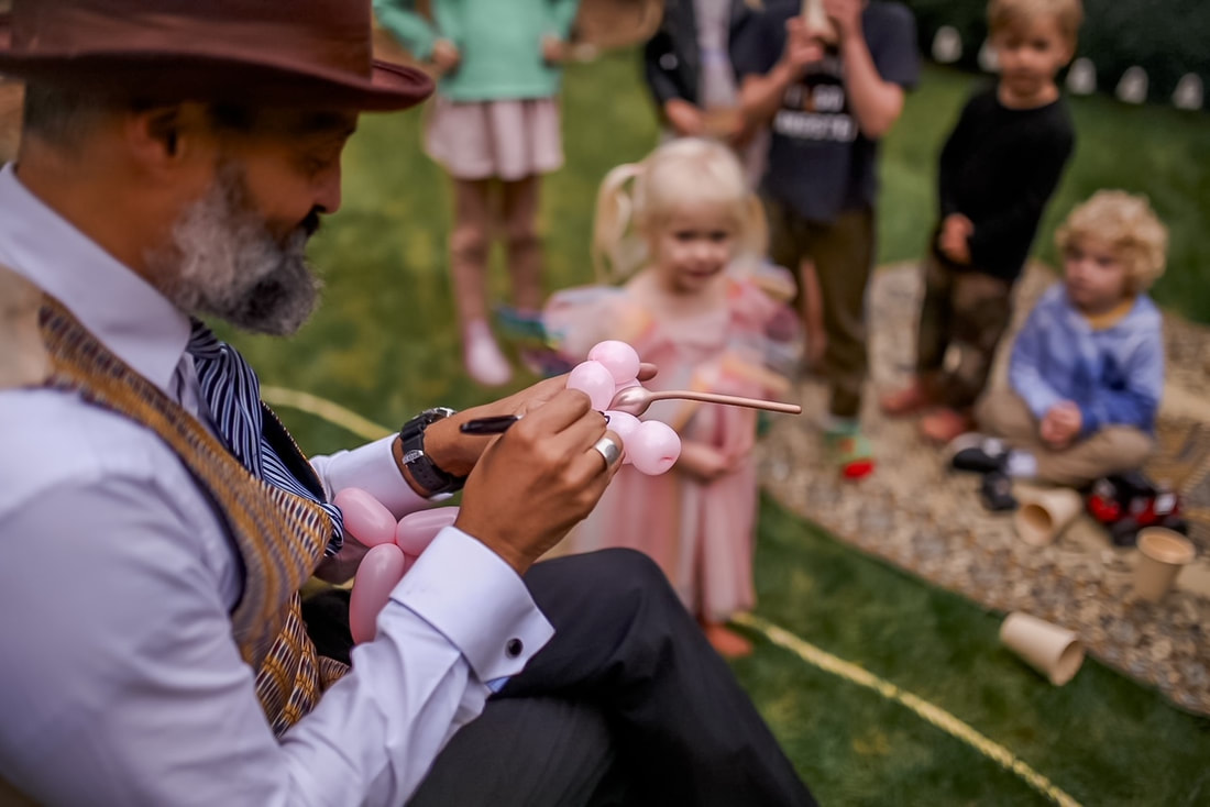 A magician draws eyes onto a balloon unicorn at a children's birthday party