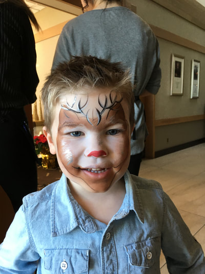 Little boy smiling and wearing Rudolph the red nosed reindeer face paint